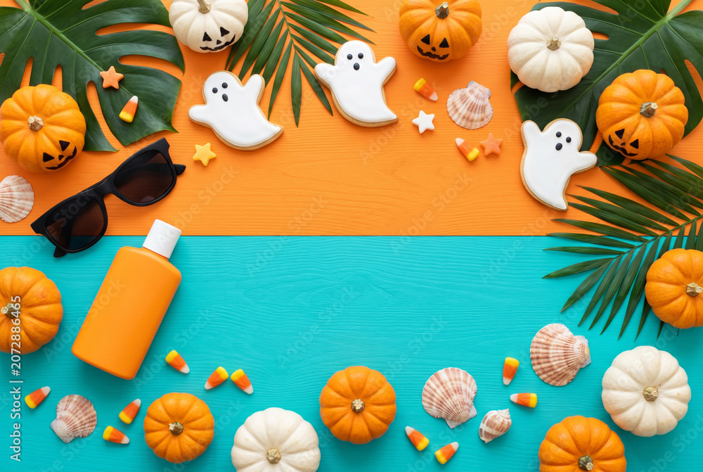 Fototapeta premium Summer halloween flat lay with pumpkins ghost cookies candy corn and tropical props for seasonal background and banner design