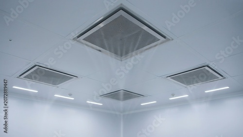 Ventilation system includes multiple square air ducts mounted on the white ceiling of a large industrial facility.