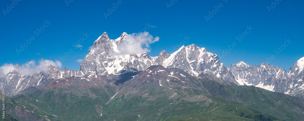 Fototapeta premium Georgia Caucasus panoramic snow capped mountain range under blue sky, alpine landscape, adventure travel, hiking destination.