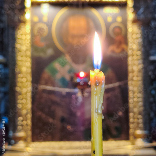 A burning candle stands in a church candlestick against the background of the icon.
