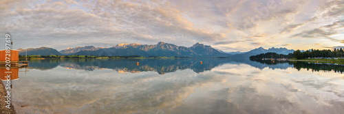 Forggensee reservoir in Bavaria, Germany, sunset sky above mountains at distance reflected on water surface