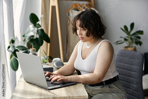 Quadro su tela Young woman focuses on her laptop while sitting in her modern, bright apartment