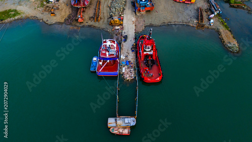 Tableau sur toile Top down vertical aerial shot of vibrant red and blue tugboats docked beside a m