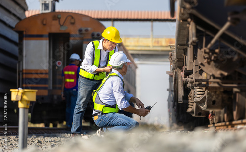 Asian railway inspector checking freight train suspension and wheel assembly at railyard, Team of Engineers in hardhat and safety vests performing maintenance inspection on cargo train equipment