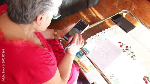  Mujer mayor con bata rosa usando un teléfono inteligente en el sofá de su casa. Mujer mayor con gafas navegando por el teléfono inteligente en casa. Senior activo, estilo de vida tecnológico moderno.