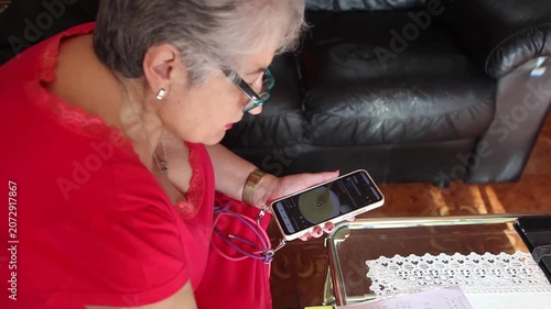  Mujer mayor con bata rosa usando un teléfono inteligente en el sofá de su casa. Mujer mayor con gafas navegando por el teléfono inteligente en casa. Senior activo, estilo de vida tecnológico moderno.