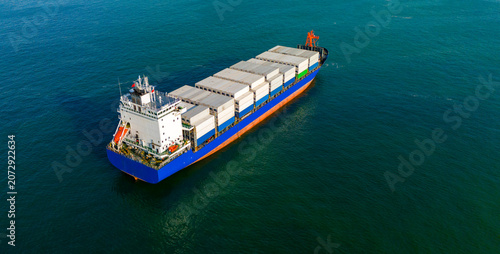 Diagonal aerial drone view of a blue and white commercial cargo ship on the ocean