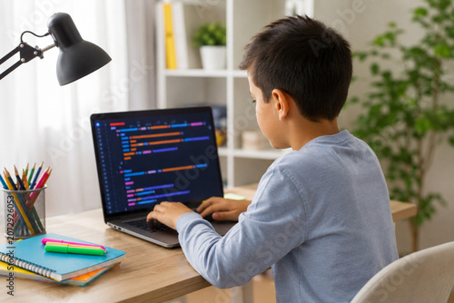 Young boy sitting at a desk learning to code on a laptop computer at home.
