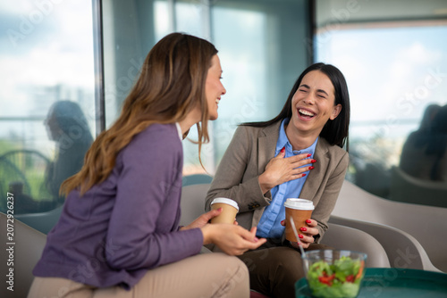 Two women laughing heartily while enjoying coffee and a healthy salad break