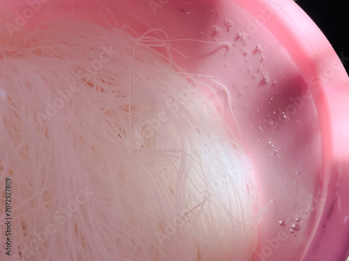 Soaking rice vermicelli noodles in water inside a pink bowl. Close up of Asian cooking preparation.