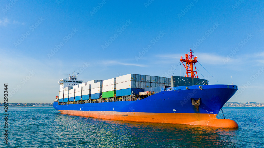 Fototapeta premium Low angle side profile drone shot of a blue cargo ship anchored near the coastline