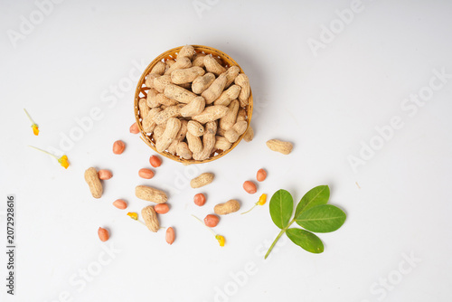 Two baskets of peanuts, one with shells and one without, arranged with scattered nuts and green leaves