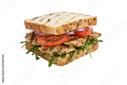Grilled chicken sandwich with fresh tomato slices, red onion rings, and green arugula leaves on toasted multigrain bread isolated on black
