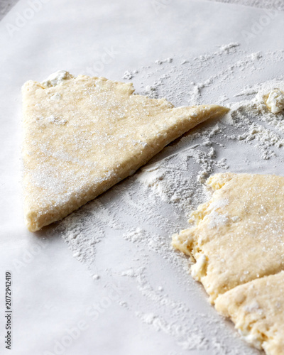 Triangular raw scone dough pieces on parchment paper with dusting of flour and sugar, preparing homemade baking