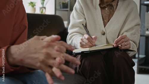 Close up of middle aged patient wringing hands during therapy session while female psychotherapist takes notes. Clip is ideal for mental health services and psychological counseling commercials