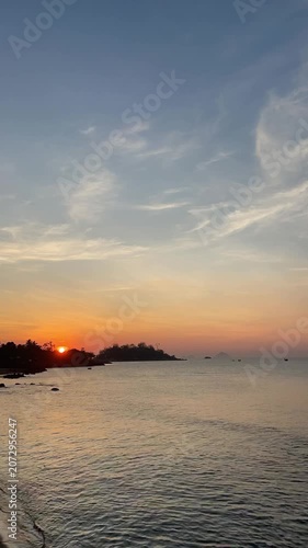 Coastal sunrise progression from predawn glow to near-morning light with sun rising left horizon over tree-covered headland and calm rippling sea