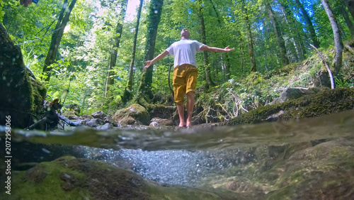 Obraz na plátně A man stands in a forest, arms outstretched, balancing on a stream in a meditative pose