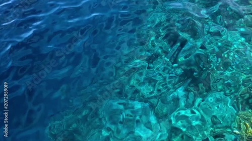 Clear blue water reveals a vibrant coral reef beneath the surface, showcasing marine life and underwater textures.