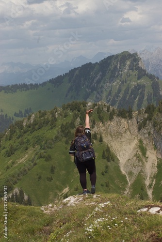 Cuadro en lienzo Back view of a girl with a backpack standing on a mountain peak and admiring the panoramic view of the alpine range on a summer day