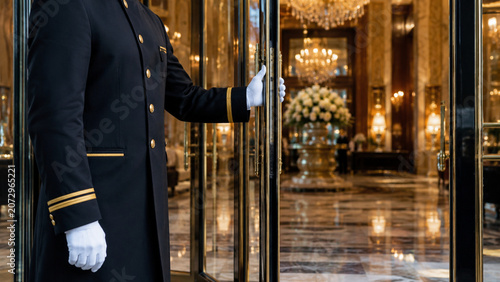 Hotel doorman opening glass door to a luxury marble lobby