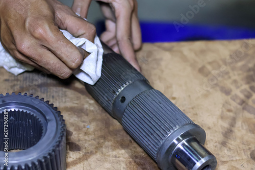 Fotografie Close up view of a technician's hands using a white cloth rag to clean a metallic transmission splined shaft component at a vehicle repair workshop