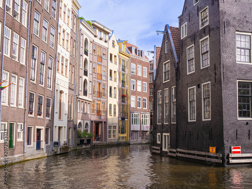 Amsterdam Damrak and Kop Zeedijk narrow canal framed by tall heritage houses, colorful facades and black brick waterfront building, summer travel view of old city architecture
