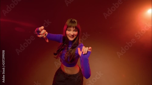 Solo woman dance pose with sharp arm accents in warm red studio lighting and dramatic nightclub mood
