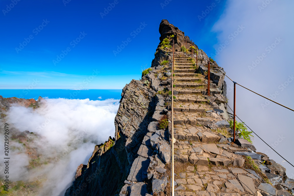 Obraz premium Ninho da Manta – a scenic trail near the summit of Pico do Arieiro on the island of Madeira, Portugal. A legendary mountain trail with steep cliffs on both sides of the path. A picturesque panorama.