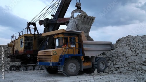 Huge mining dump truck moving stones in an open-pit quarry against a blue sky background