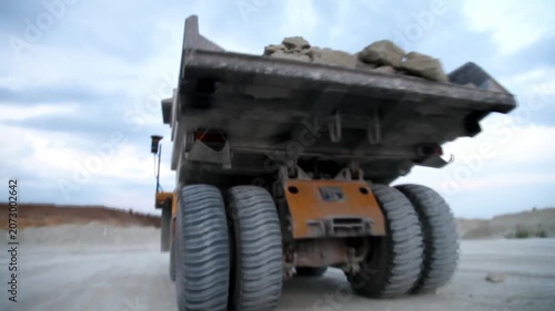 Huge mining dump truck moving stones in an open-pit quarry against a blue sky background
