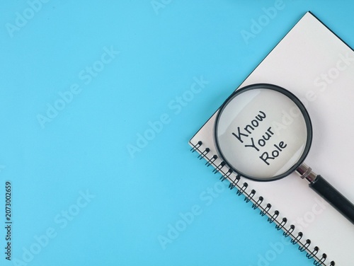 Magnifying glass focusing on the handwritten text Know Your Role on a book against blue background, Suitable for business, management, team collaboration, and accountability concepts