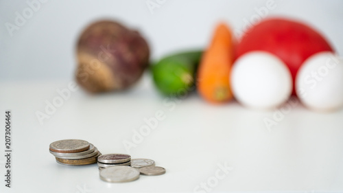 Tableau sur toile Saving money on groceries concept with stack of coins and blurred fresh food