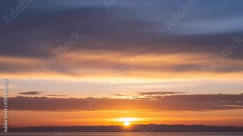 Sunset over ocean with cloudy sky.