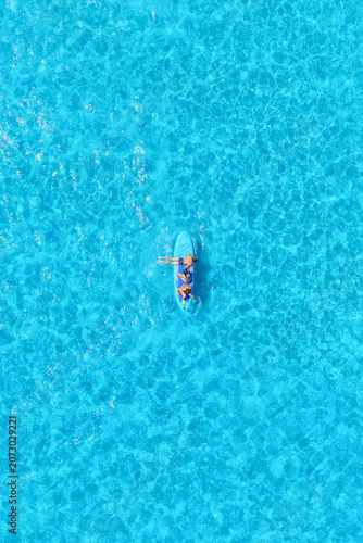 Vertical aerial drone view of friends having summer fun on SUP boards, surfing and jumping into the sea waves. Group of people playing and relaxing together in the turquoise water.