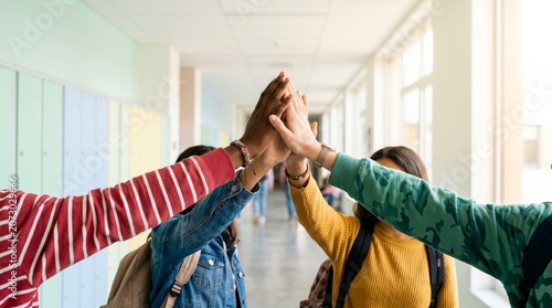Group of diverse students high-fiving in school hallway together  