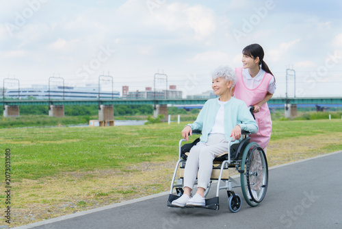 土手を散歩する車椅子に乗った日本人シニア女性と若い日本人介護士の女性