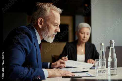 Photos Middle aged business executives reviewing documents during oil industry meeting, discussing strategy and financial planning