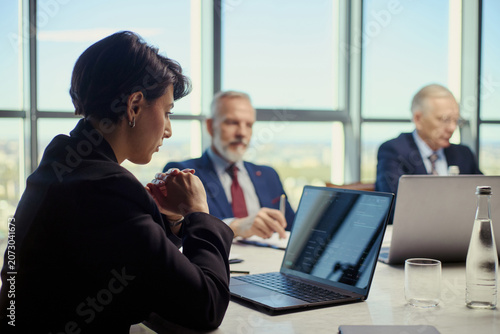 Фотография Middle aged businesswoman leading oil industry meeting, reviewing laptop data with senior businessmen, discussing strategy and investment
