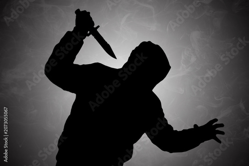 Mysterious dark silhouette of a hooded figure holding a knife, presented against a moody, smoky background