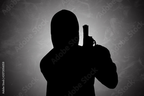 Mysterious dark silhouette of a hooded figure holding a handgun, presented against a moody, smoky background