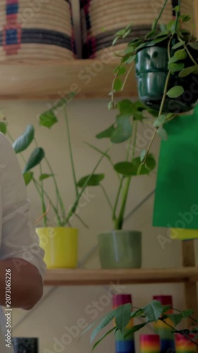 Vertical video: Checking tablet white tee person checking plants on shelves at home to confirm care