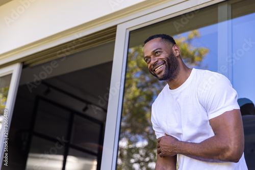 African man wearing whitetee leaning on sliding door at home smiling outward, copy space