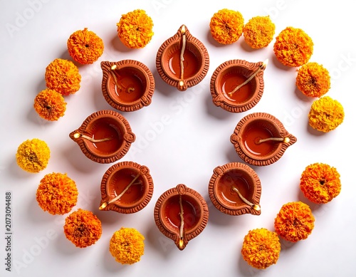 A circular arrangement of clay diyas surrounded by orange and yellow flowers on a white surface