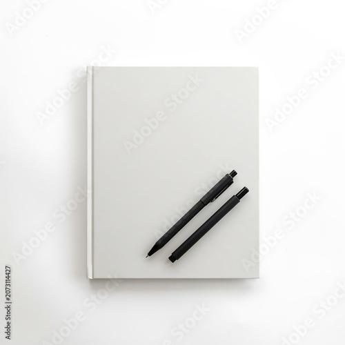 Minimalist Vertical White Notebook Mockup with Black Pens on White Surface.