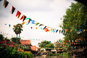 Colorful triangular bunting flags strung over a lush tropical canal village at a festival in Thailand