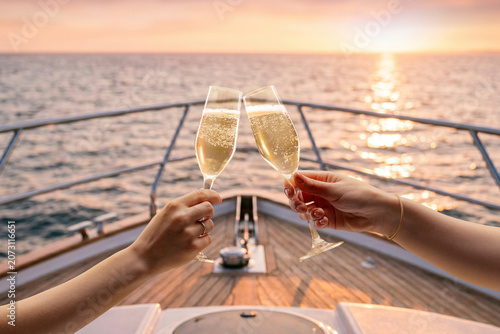 Hands toasting champagne glasses on luxury yacht during sunset cruise. Concept of yacht charter advertising, luxury travel, honeymoon vacation and celebration campaign.