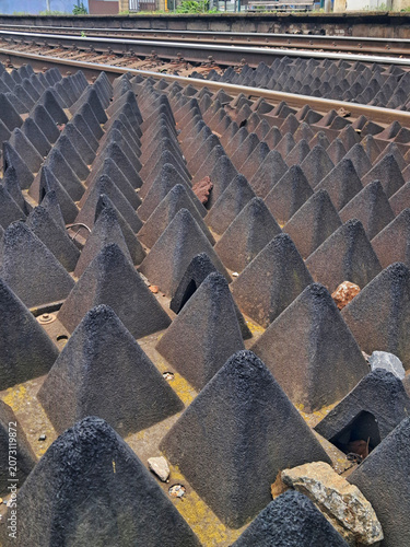 Black rubber tactile anti trespass panels with sharp pyramid shapes installed on a train railway track to prevent people from crossing.