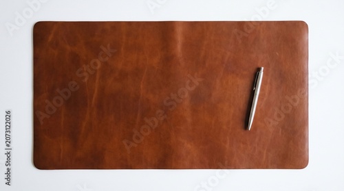 A large leather desk mat in warm cognac/tan brown with natural grain texture and subtle variations, photographed flat against a white background. A single silver ballpoint pen is placed vertically.