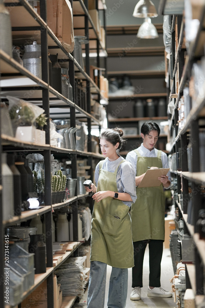 Fototapeta premium A saleswoman and salesman do a display check in the homeware aisle, the young woman cradling her clipboard while the young man inspects a tall glass vase against the light