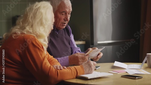 Senior man and his wife reading overdue bills and calculating household expenses